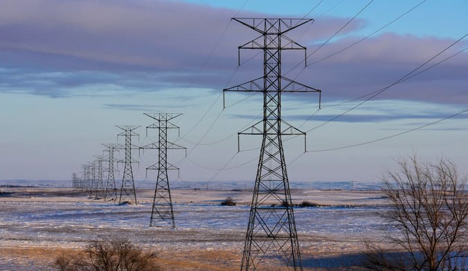 A row of large transmission towers in a snowy prairie landscape