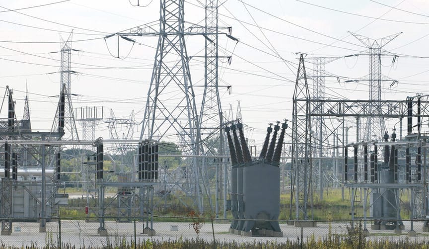 large gray metal transformers and power transmission lines in a fenced outdoor lot