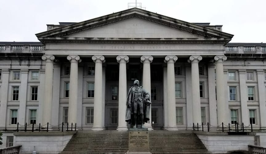 The front facade of the US Treasury building in Washington DC. In the foreground is a statue of a man.