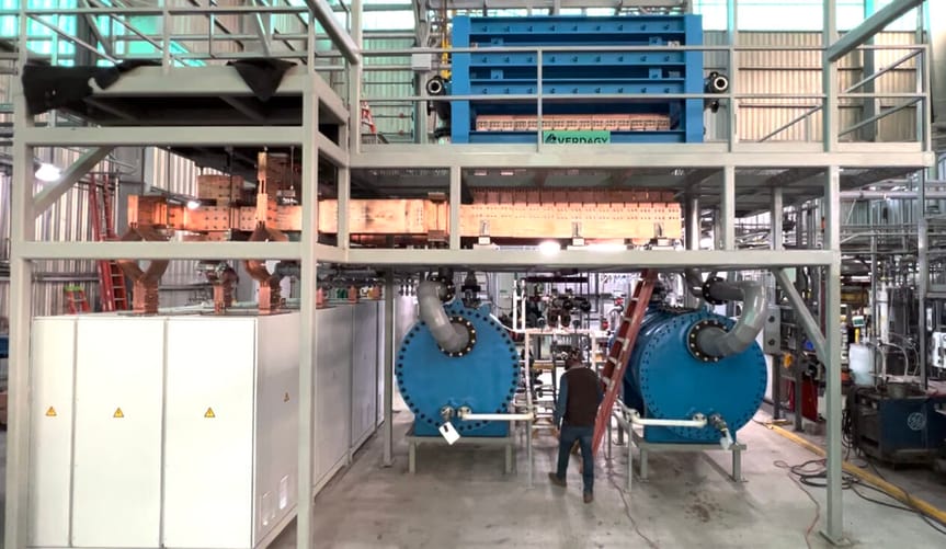a worker in safety walks through a large industrial facility full of pipes and equipment