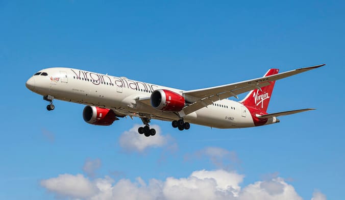 A white and red plane that says Virgin Atlantic flies in the sky