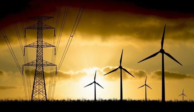 A transmission power line and several wind turbines are seen in stark silhouette against the backdrop of a sunset