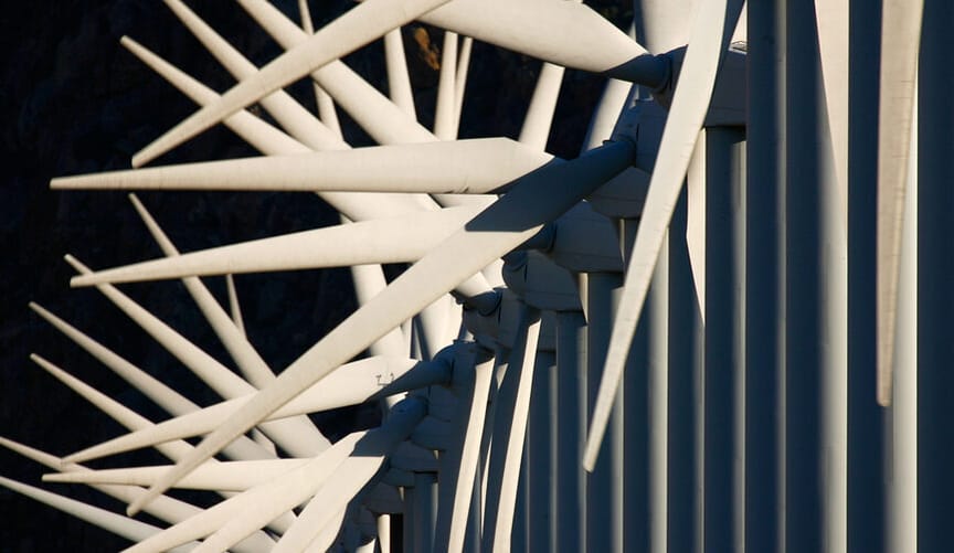 A large row of white wind turbines with blades out of sync, giving them a spiky appearance