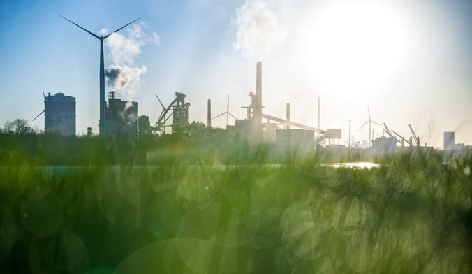 In the foreground is a green grassy field with bokeh lighting effect, in the background is a large industrial site