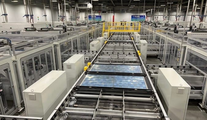 Blue rectangular solar panels move along an automated assembly line in a very large industrial facility