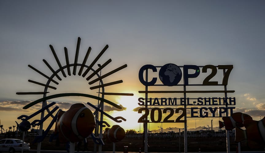 A sign that says COP27 SHARM EL-SHIEKH EGYPT 2022 in front of a sunset