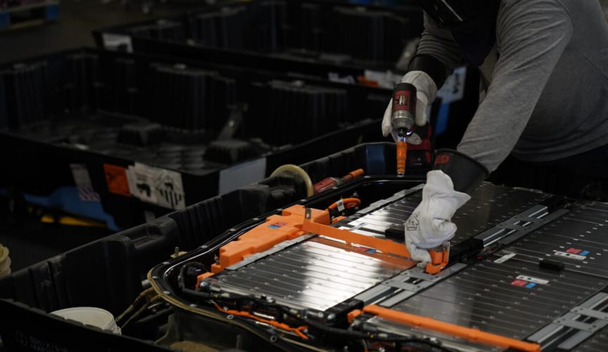 A worker uses tools to take apart silver lithium-ion cells from a battery module