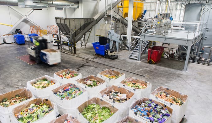 Crates of expired fruits and vegetables sit on the floor near factory equipment