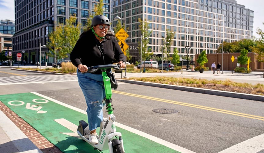 A person rides a lime electric scooter down a bike lane in a city