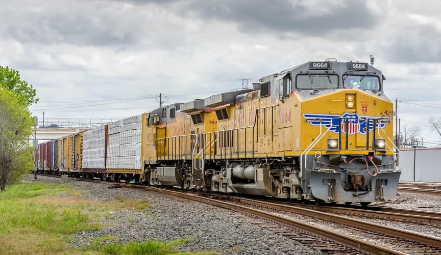 A yellow locomotive with a Union Pacific logo pulls rail cars down the train tracks