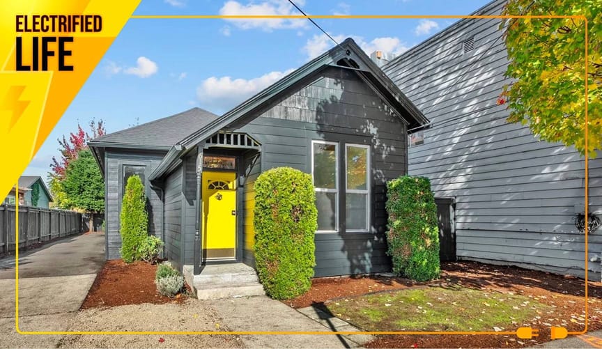 1-story gray house with slanted roof, yellow door, covered entryway, and green bushes.