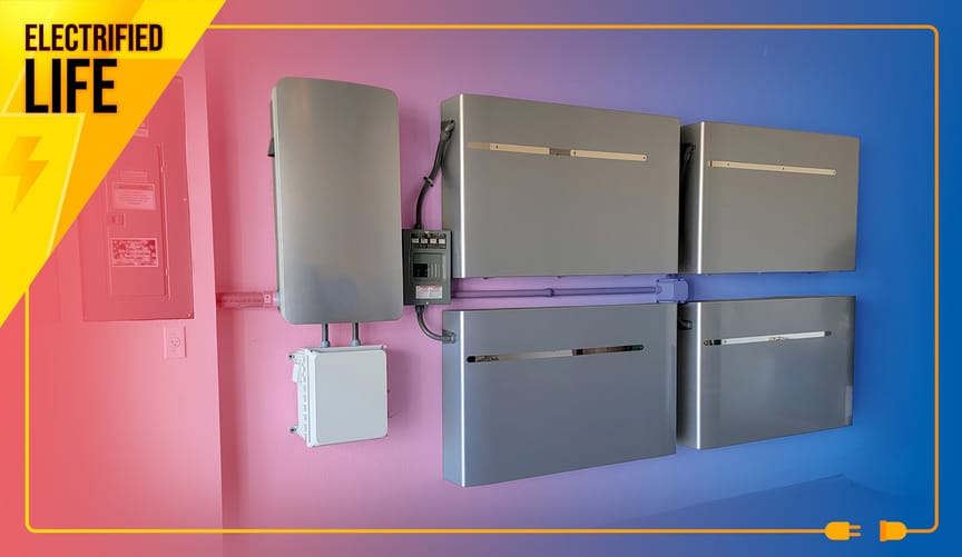 Four silver-colored boxy batteries with auxiliary systems line a garage wall.