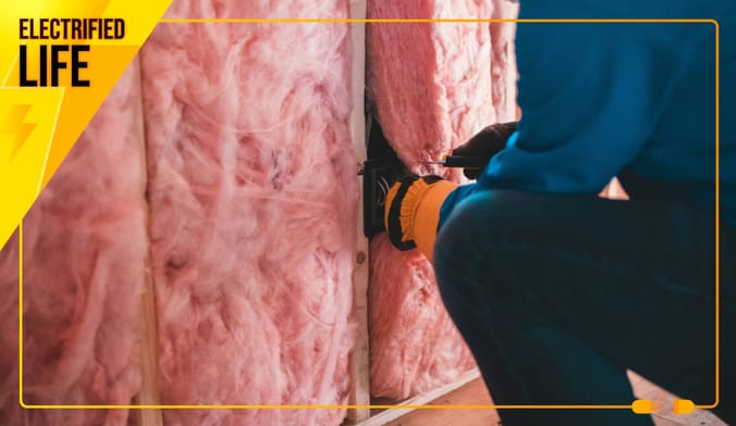 Person in blue installing pink fiberglass insulation