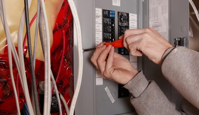 A person installing a grey electrical panel or breaker box.
