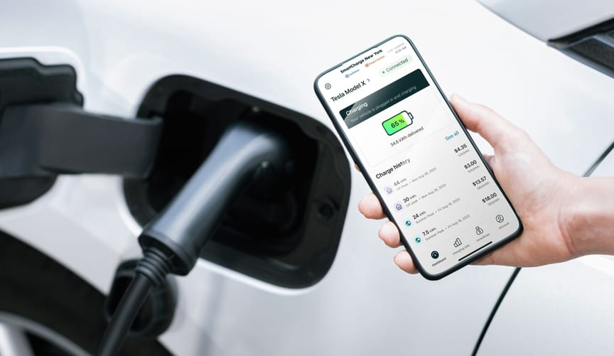 A hand holding a phone with a mobile app with charging status and incentive options for a Tesla plugged into an EV charger