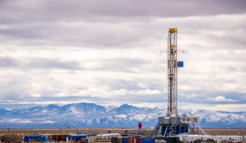 An industrial drilling site in the desert in front of a snowy mountain range