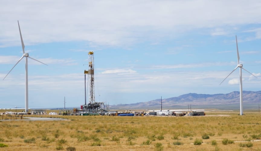 An industrial site in the desert flanked by two wind turbines
