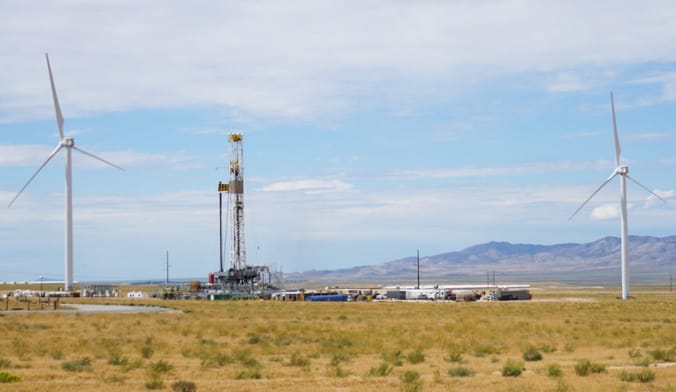 An industrial site in the desert flanked by two wind turbines