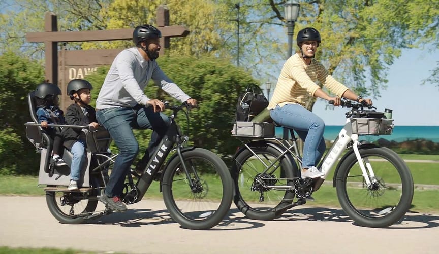 A man, a woman, and two children ride on a park bike trail on electric bikes