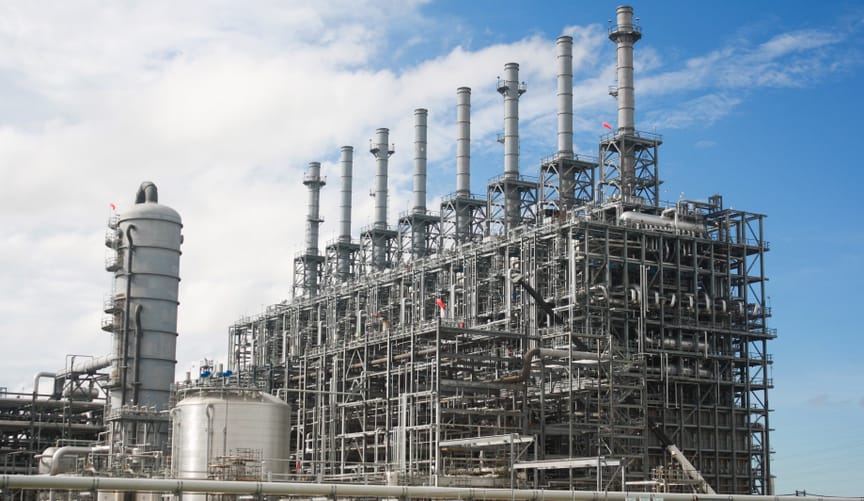 A large industrial facility with a row of skinny metal  smokestacks pointing up into the blue sky