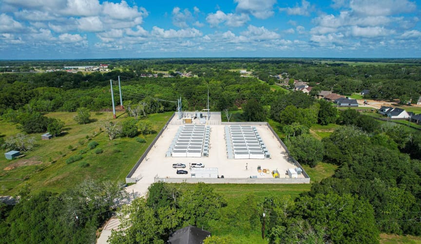 An aerial view of a energy storage facility consisting of rows of large rectangular white metal boxes