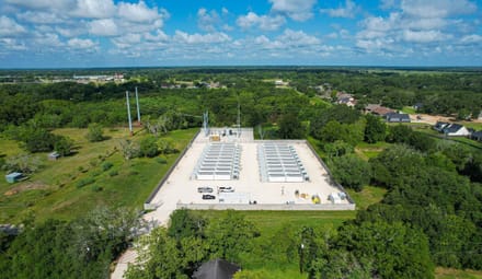 An aerial view of a energy storage facility consisting of rows of large rectangular white metal boxes