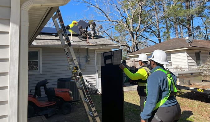 Workers installing solar panels on a small white-paneled home