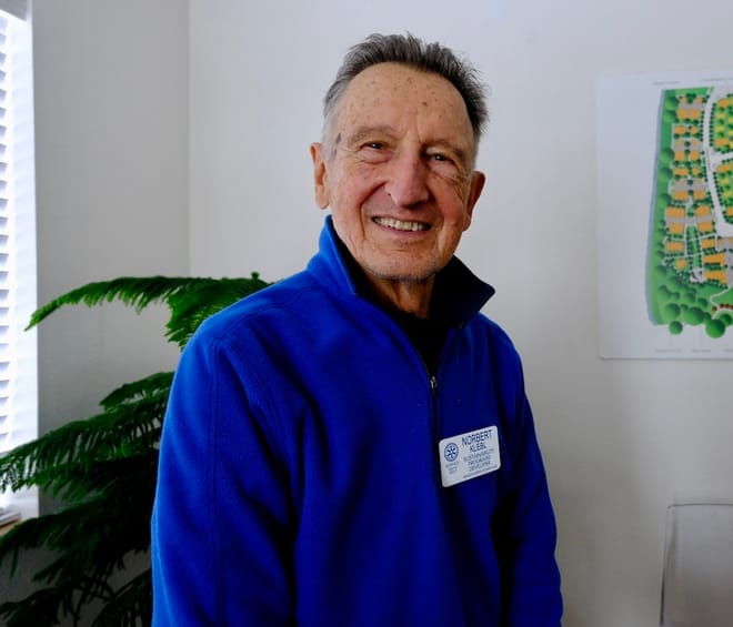Smiling man with close cropped dark brown and grey hair in blue pullover.