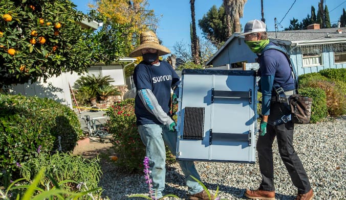 workers carrying a battery through a yard