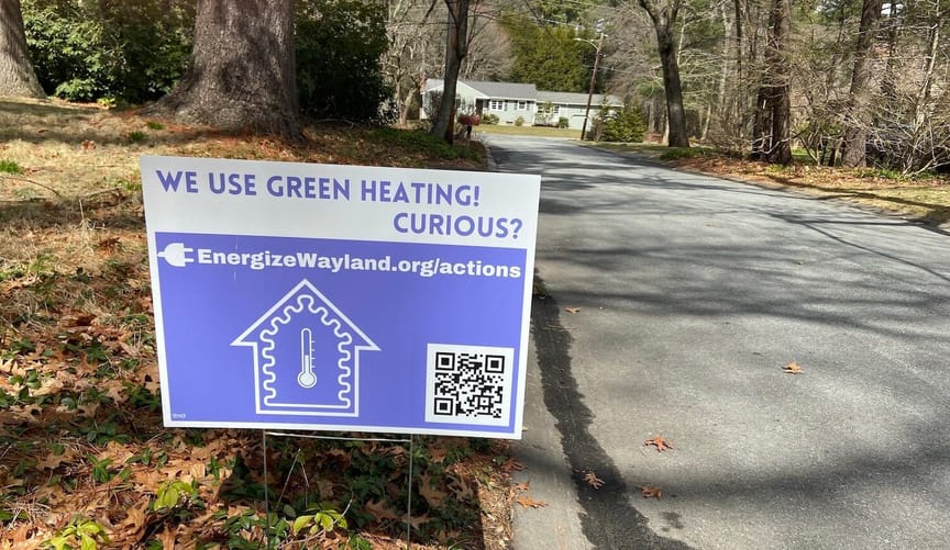 Yard sign on lawn with fallen leaves says "We use green heating! Curious?" and a url: EnergizeWayland.org/actions
