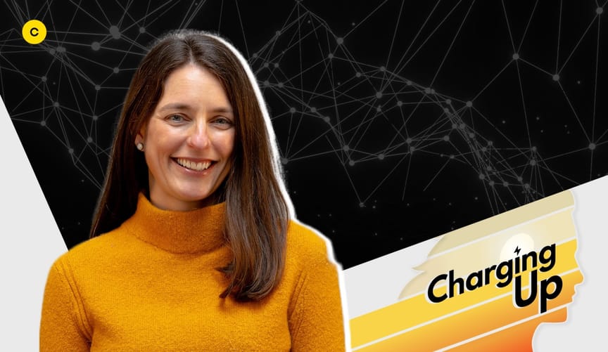 A smiling white woman with shoulder length brown hair in an orange turtleneck sweater. A stylized graphic says Charging UP