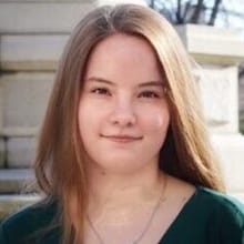A woman with light skin and medium brown, shoulder length hair wearing a green blouse