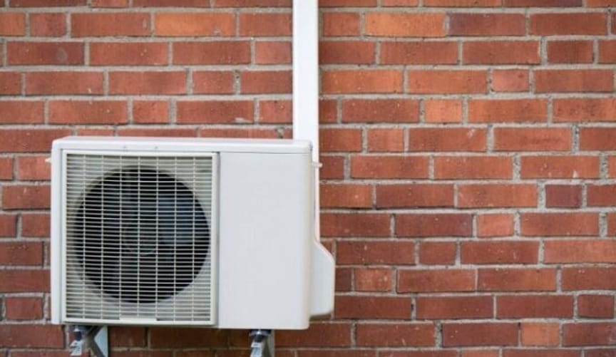 A white metal heat pump attached to a red brick exterior wall