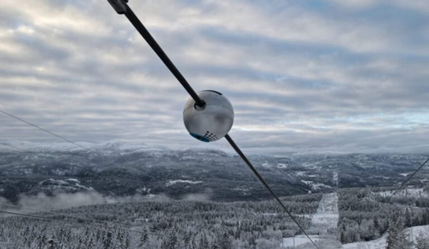 A Heimdall Power sensor on a transmission line crossing a wintry landscape