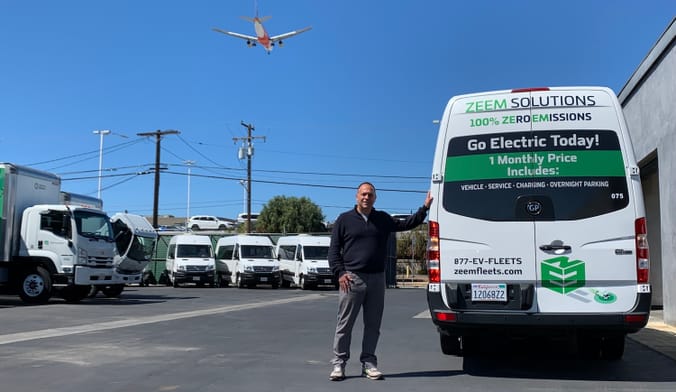 Zeem CEO Paul Gioupis shows off an electric van available for lease as a plane descends to nearby LAX.