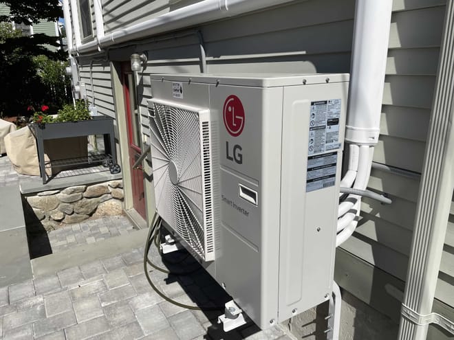 A side view of a beige LG heat pimp attached to a house with beige siding