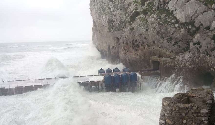 Eight blue wave power devices sit in the ocean in front of a large brown rock