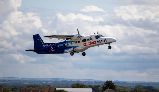 A blue and white propeller aircraft flies over a green countryside