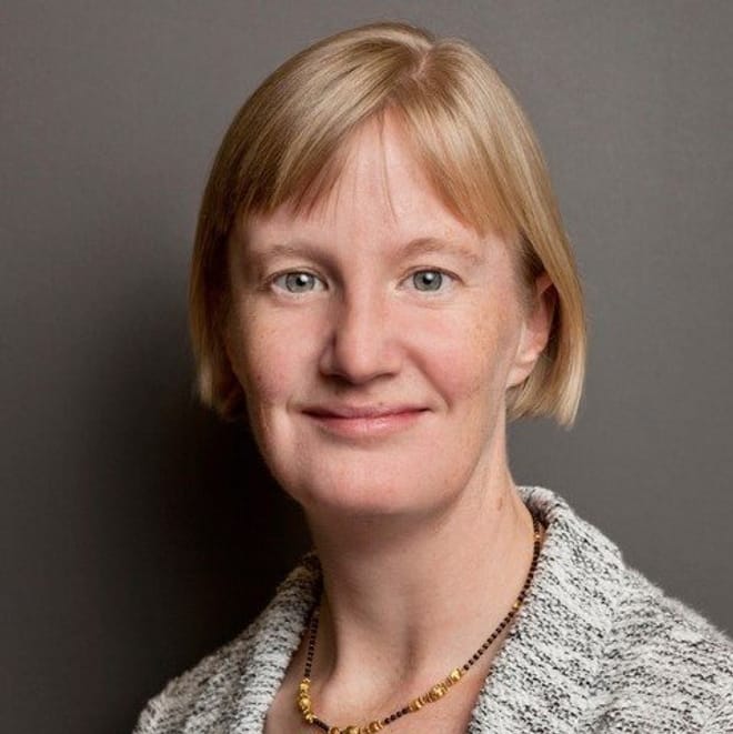 A smiling woman with a light skin tone and a short strawberry blonde bob haircut wearing a gray heathered jacket