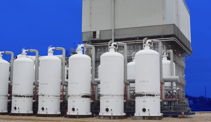 Several large pieces of industrial equipment flanked by a row of vertical white cylindrical metal tanks.