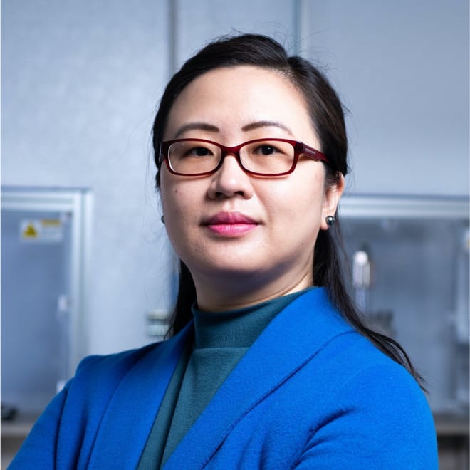 An Asian woman with a light skin tone and shoulder length dark hearing wearing brown glasses and a blue jacket