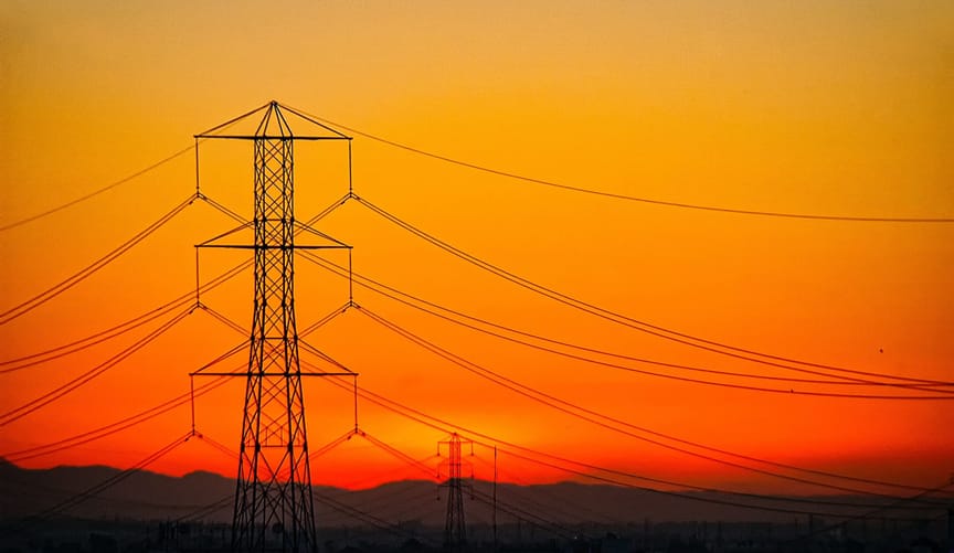 A large transmission tower and power lines set against the backdrop of a blazing orange sky