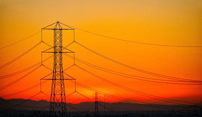 A large transmission tower and power lines set against the backdrop of a blazing orange sky