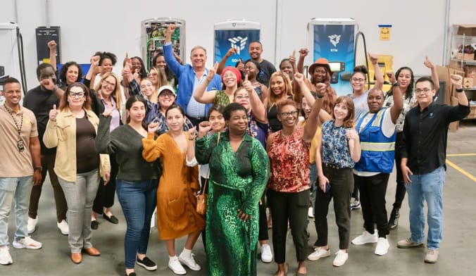 A group of men and women stand with their fists raised. Electric-vehicle charging stations are in the background