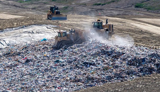 Trash is flattened and spread out across a hilllside before being covered with dirt at a landfill in San Juan Capistrano