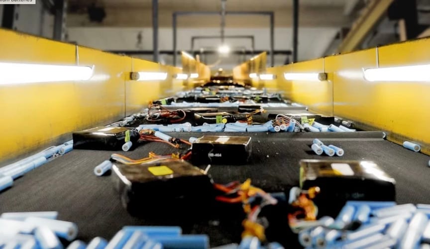 Various types of used batteries on a conveyor belt in a large manufacturing facility