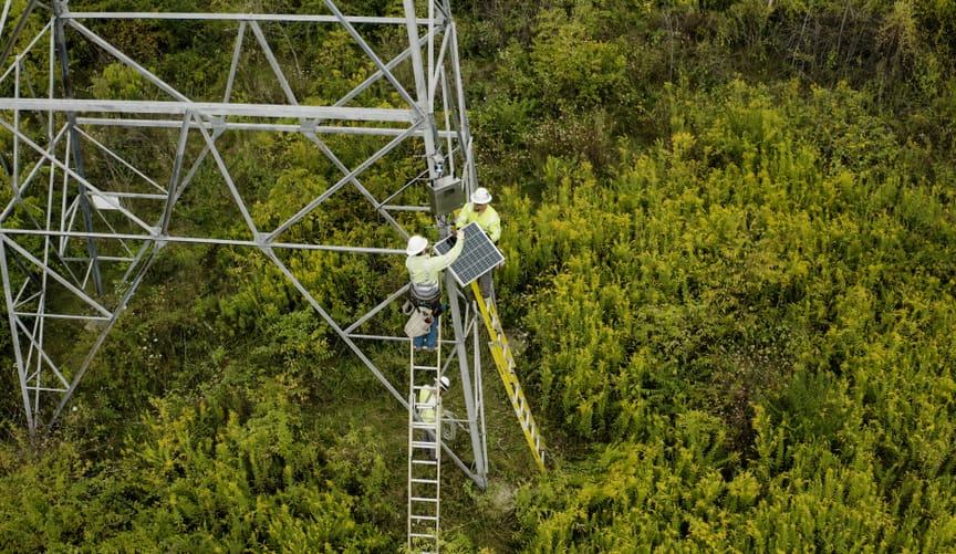 Workers install a LineVision dynamic line rating sensor at the base of a transmission tower.