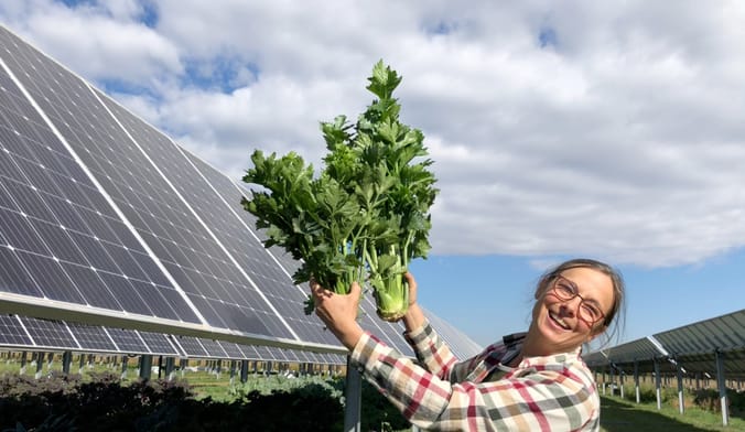 Woman with glasses holds up celery in front of solar panels and blue sky