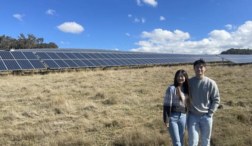 A man and a woman stand in the foreground, a large solar array is behind them