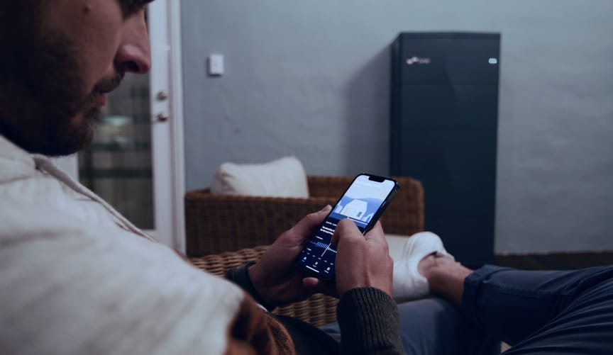 Man holding smartphone displaying Lunar Energy app, with Lunar Energy battery/inverter in the background